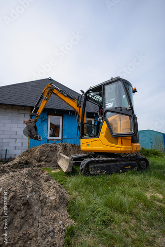 An excavator is digging near a house with blue walls while workers plan for an ongoing renovation project in the daytime