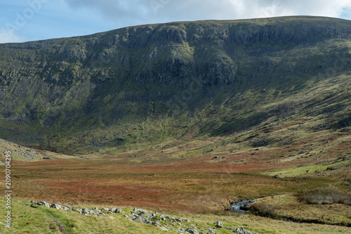 Bild auf Leinwand Expansive mountain valley with grassy slopes, rocky crags and a small stream in the Lake District