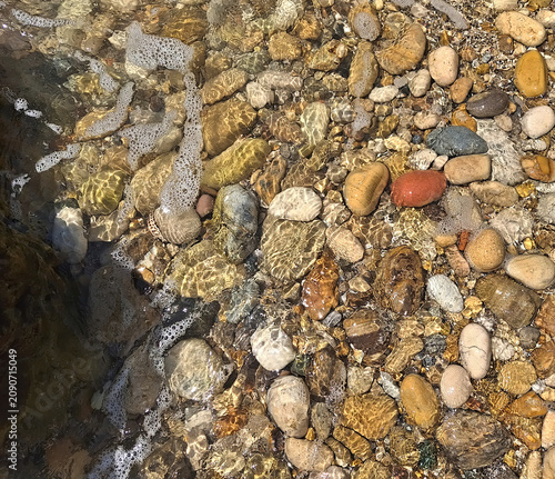 golden and sunny view of small pebbles underwater on the seashore