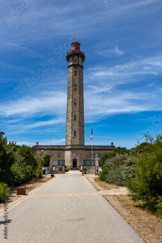 Visitors on the path leading to the historic Phare des Baleines lighthouse with a French flag on a sunny summer day in Ile de Re, France
