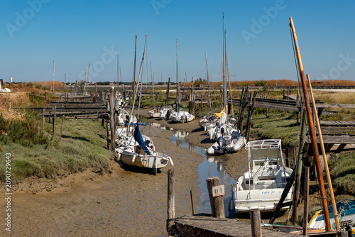 Small white boats stranded in the thick mud during low tide in a traditional salt marsh channel with rustic wooden piers in Ile de Re, France.