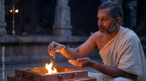 Indian priest performing fire ritual - Elderly man performing ritual offering by fire in temple setting  