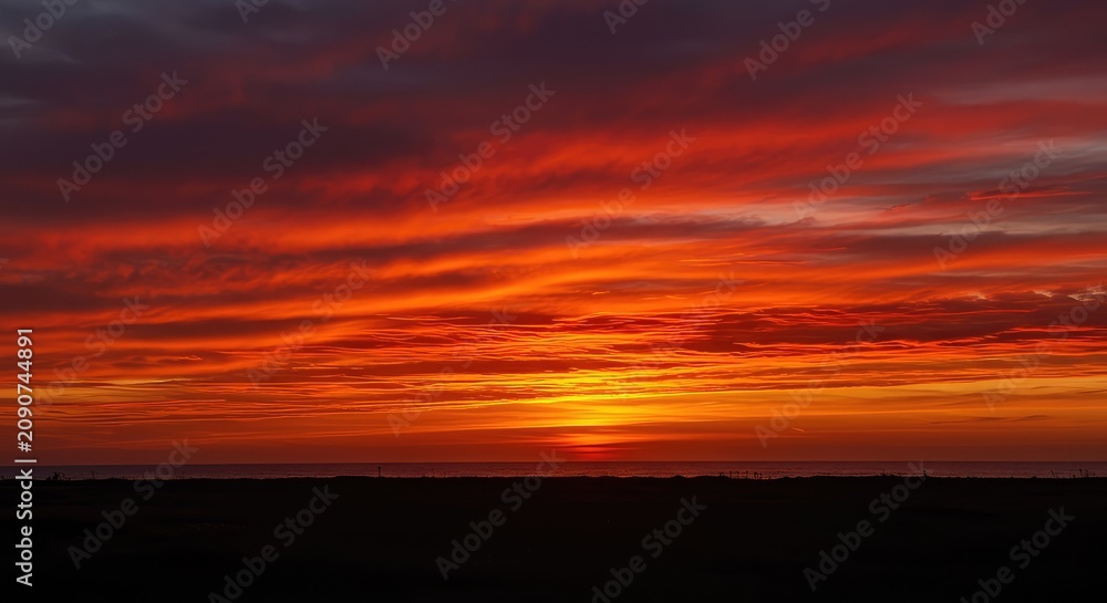 Fototapeta premium A dramatic, fiery red sunrise painting the early morning sky with intense orange and crimson hues over a tranquil horizon ,glowing ,solar ,climatic