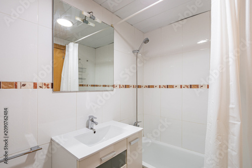 Modern bathroom with a shower, white tiles, and a mirror. Features a sink and a bathtub. Clean and minimalistic design