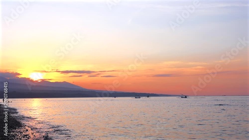 Sunset over ocean and black sand beach with traditional outrigger boats in Bali.