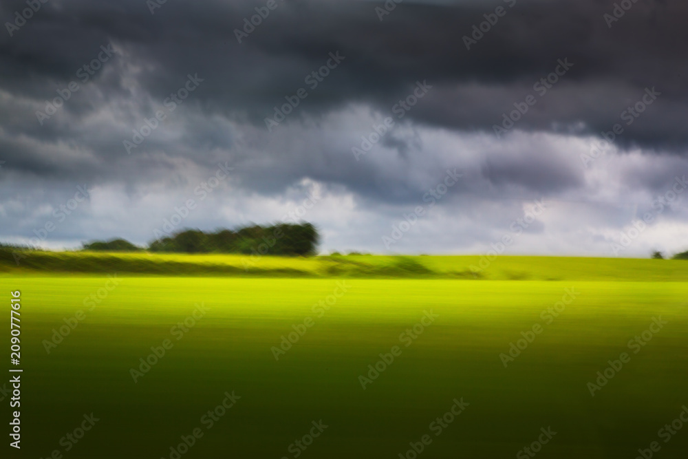 Fototapeta premium art Nature in motion from train window, abstract blur with dramatic storm sky over green field
