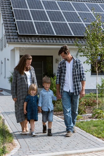 Happy family looking at their modern house with solar panels on roof, sunset.