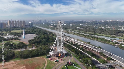 Cinematic wide orbital drone shot circling the Ferris wheel at Villa-Lobos Park on a beautiful sunny day with a vibrant blue sky. Aerial footage showcasing the landmark within one of São Paulo's most