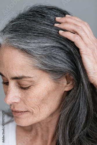 Woman showing gray hair roots while touching her head close up. Aging and hair care.