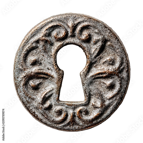 A close-up view shows a vintage keyhole plate made of decorative metal. This piece features an old design with intricate details and a worn appearance. It rests on a smooth surface