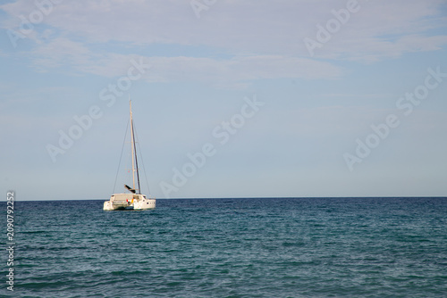 Catamaran sailing on calm blue ocean waters under a clear sky with soft clouds in the background, creating a serene maritime scene
