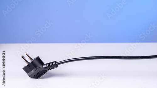 Konstfotografi Black plug with two metal prongs rests on white surface
