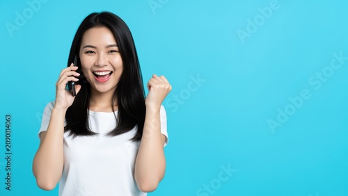 Excited Woman on Phone: A young Asian woman beams with joy and excitement while speaking on her smartphone.