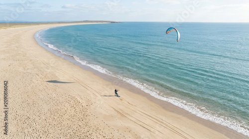 Kitesurfer riding on a board along a sunny sandy beach with blue ocean water on a clear summer day in the outdoors