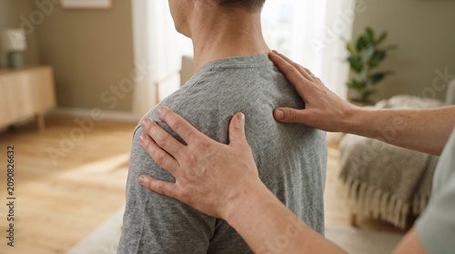 Hands of therapist massaging man's shoulders at home for pain relief and wellness.