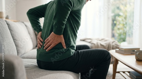 Senior man holding lower back in pain while sitting on living room sofa