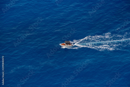 Aerial view of a motorboat gliding through a blue bay, leaving a white trail behind it. Zakynthos island, Greece.