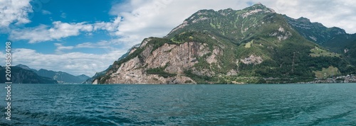 Fotografie Large panorama from the Untersee (Lower Lake Constance) with the old Axenstrasse road and Flüelen under a blue sky with white clouds