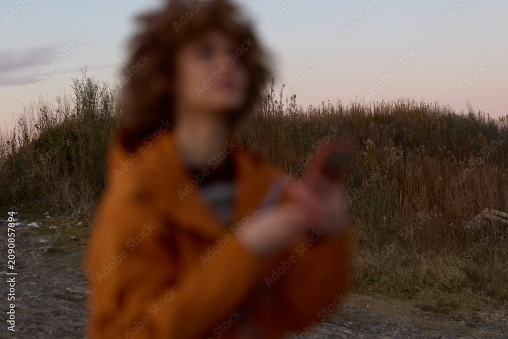 Fototapeta premium Woman lifestyle outdoors in field at sunset, blurred tall grass and path, woman in warm coat, soft bokeh light, calm nature mood, cinematic portrait