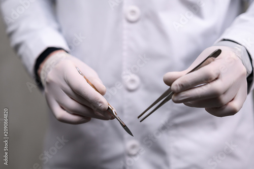 Fotografija Surgeon holding scalpel and forceps in sterile gloves before surgical procedure