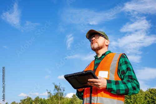 Foto Climatologist or environmental supervisor in protective uniform analysing weather data on a digital tablet in front of a green forest and blue sky