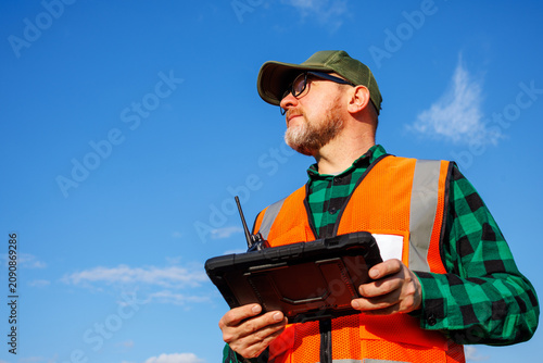 Obraz na płótnie Environmental engineer or field supervisor conducting land monitoring and data collection using rugged digital tablet under blue sky