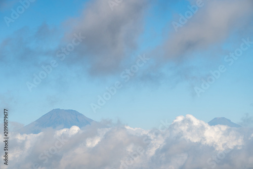 Active stratovolcano located in Indonesia. This view shows mountain peaks towering above the cloud cover under a blue sky.