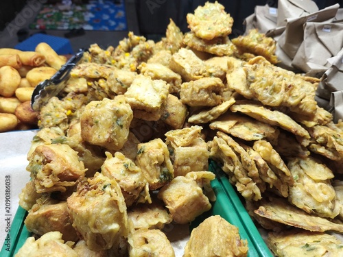 A pile of various traditional Indonesian deep-fried snacks, known as gorengan, including fried tofu, tempeh, and vegetable fritters, neatly arranged on a tray at a street food stall.