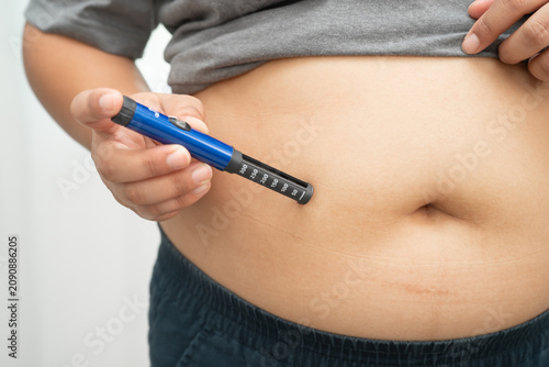Asian woman injecting herself diabetes injecting insulin in stomach at home.