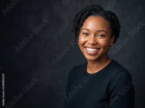 A beautiful woman with a radiant smile, her dark hair styled in twists, looking confidently towards the camera against a dark, textured background