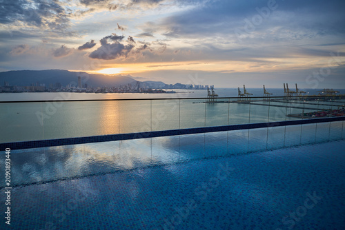 Luxury infinity swimming pool overlooking waterfront city skyline at sunset