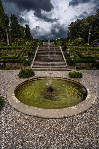 Formal gardens of Miramare Castle near Trieste, Italy. Elegant European landscaping with symmetrical fountain and dramatic sky.