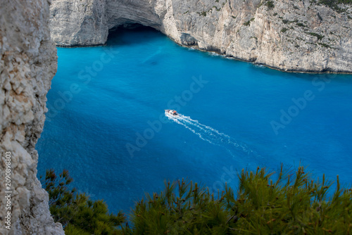 A small motorboat crosses a turquoise bay at the foot of limestone cliffs.