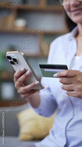 Vertical woman holding credit card and using smartphone for online shopping, entering payment details for transaction on internet, mobile banking, digital payment, pay bills, spending money. Close up.