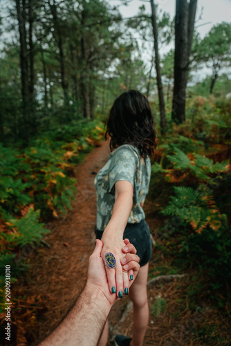 Fotografía Romantic Couple Holding Hands Walking Through Trail Surrounded by Ferns and Pine