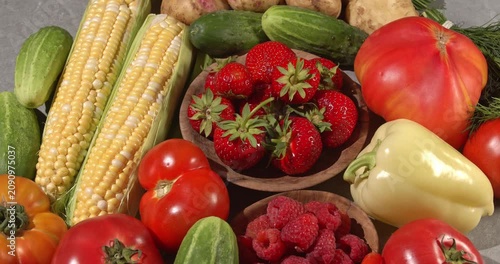 Fresh healthy products on a gray table. Close-up footage of  corn, strawberries, cucumbers, tomatoes, green onions, potatoes, raspberries, dill, sweet peppers on a rotating table.
