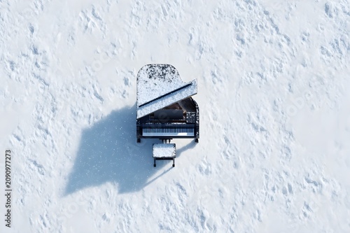 Photorealistic aerial top view of a grand piano standing alone in fresh white snow, perfectly centered composition, piano partially covered in snow, fine snowflakes falling, winter landscape