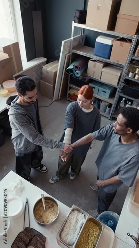 Vertical video of diverse young adult volunteers putting hands together in team stack inside food bank. Footage is perfect for social diversity and community support campaigns