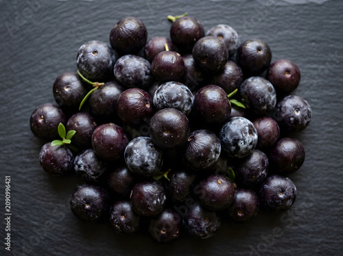 Overhead macro flat lay of fresh açaí berries on dark surface showing deep purple skin texture, Brazilian superfood concept