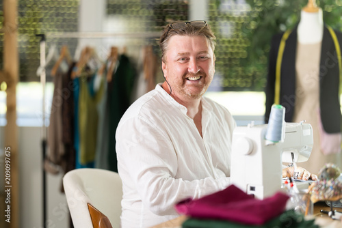 Happy middle-aged male dressmaker working with sewing-machine
