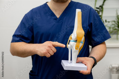Healthcare professional holding anatomical knee joint model during orthopedic consultation