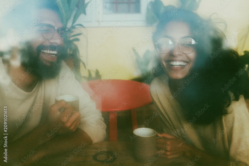 Fototapeta premium A young Indian couple laughing over coffee in a bright sunlit room, their candid joy and warm amber tones creating a cozy intimate mood for lifestyle and home leisure visuals