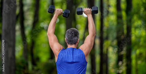 Strong man do sport exercise. Outdoor workout. Sport athlete man with dumbbell. Healthy lifestyle. Biceps muscle. Strong triceps. Man exercising with dumbbell. Man athlete lifting dumbbell, back view