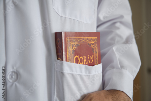 Person carrying the coran in a white lab coat pocket, symbolizing faith and profession