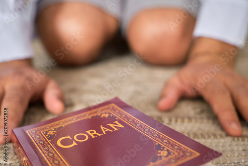 Muslim person is prostrating during prayer with the holy quran on a mat