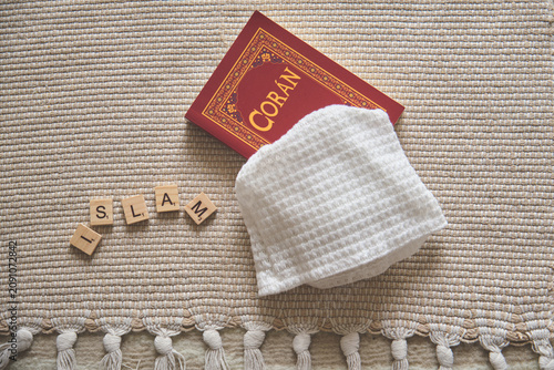 Islamic holy book, prayer kufi and scrabble tiles spelling islam on a prayer rug