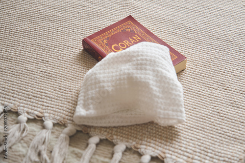 Coran book and a white kufi cap resting on a beige woven prayer rug