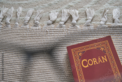Coran, the holy book of islam, resting on a beige prayer rug with fringes
