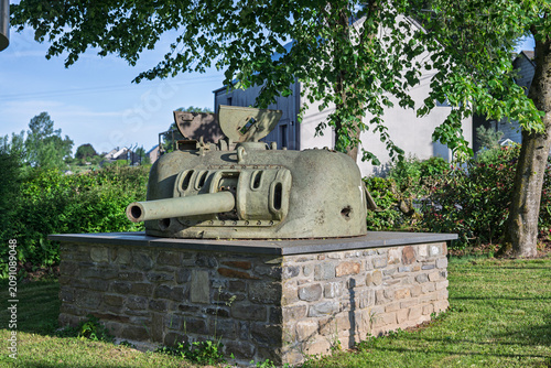 Historical World War II American tank turret monument on a stone pedestal by an information sign in the village of Marvie near Bastogne, Belgium.
