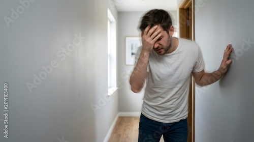 Exhausted man leaning heavily against a white wall feeling dizzy